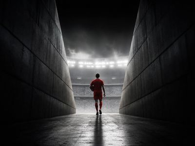 Eenzame voetballer in een rood shirt, op de rug gezien, stapt vanuit een donkere stadiontunnel richting fel licht
