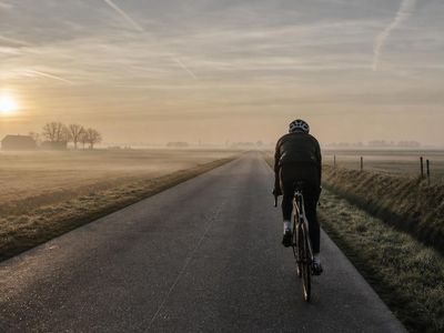Eenzame wegfietser op een mistige Vlaamse landweg bij zonsopgang